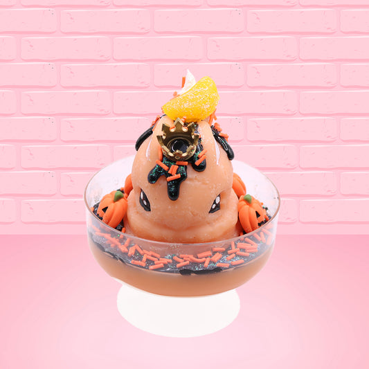 Cute kawaii Pumpkin King Bunny orange ice cream sundae with black glaze, orange sprinkles and pumpkin faces in the dish. The bunny has a golden crown and orange slice on top next to the swirl of whipped cream. This view is from the front.