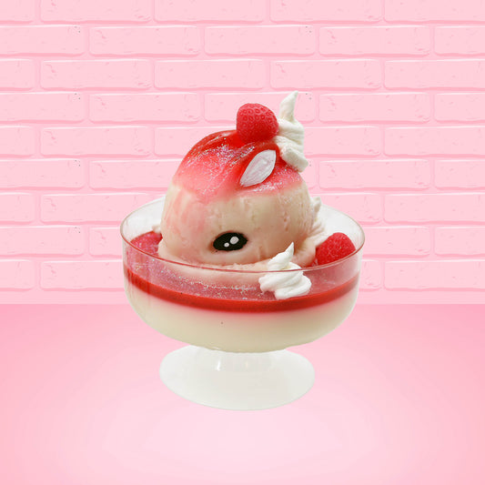 Cute kawaii bunny strawberry cheesecake white ice cream with red glaze, strawberries, and whipped cream swirls in the dish. The bunny has a strawberry on top between the ears, with a swirl of whipped cream on the back. This view is from the front at an angle.