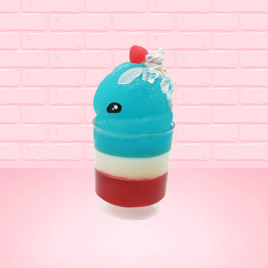 Cute kawaii bunny blue ice cream tall sundae that has red, white and blue layers in the dish and a strawberry on top near the whipped cream and pearls. The photo is taken from the side.