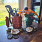 Desk setup with a decorative container holding tools in the tool cup in use, a figurine, and various small objects on a wooden surface.