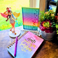 Example display of Moon and Star enamel pin board with an anime girl figure on a desk next to plants and a journal that says create your own sunshine.