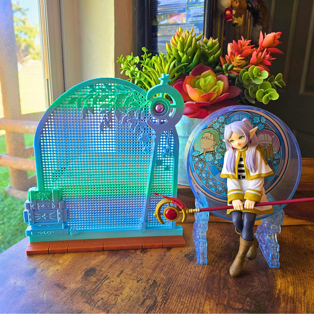 Silk Ice Blue Frieren Window enamel pin board next to a sitting anime girl figure on top of a desk in a room. 