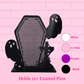 Black coffin-shaped mesh pin holder with ghost-shaped side cutouts, shown against a pink brick wall background with color options labeled White, Lt Pink, Purple, and Black, plus text stating 'Holds 12+ Enamel Pins'.