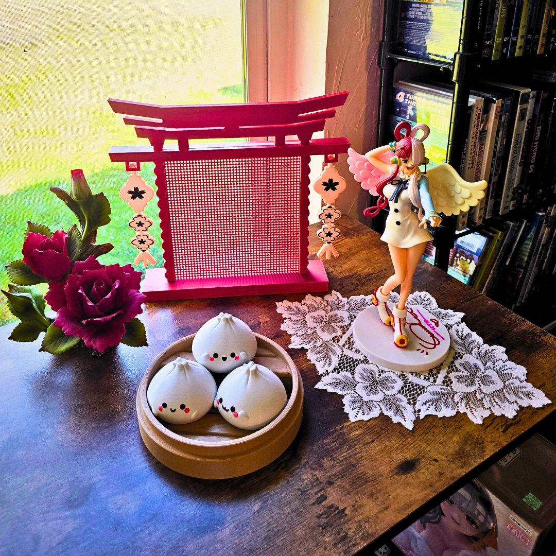 Japanese Arch Enamel pin board on top of a desk next to girl anime figure, flowers, hot dumpling toy by a window.