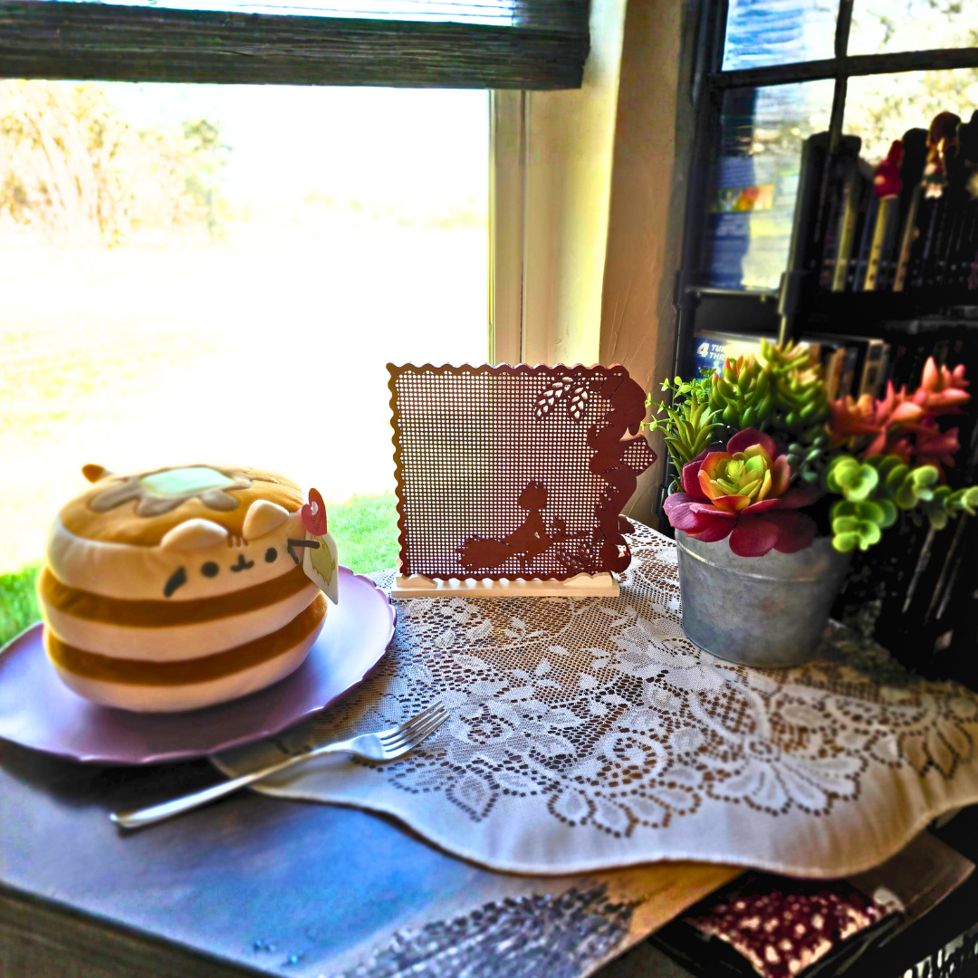 Bread Brown Kiki’s Bread Bakery enamel pin display on top of a doily, next to a cute cat pancake plush on a purple plate at another angle.