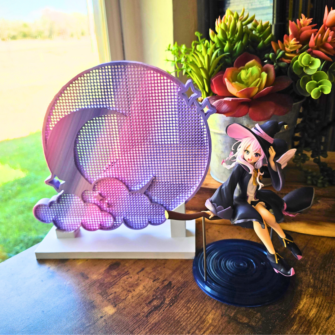 Angel Sky Moon and Cloud enamel pin board next to an anime girl figure on a broomstick, and on a top of a desk in a room. 