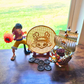 Gold pirate bunny coin enamel pin display board next to some pirate coins and a pirate ship on top of a desk.  An anime guy figure is near the enamel pin board as well 