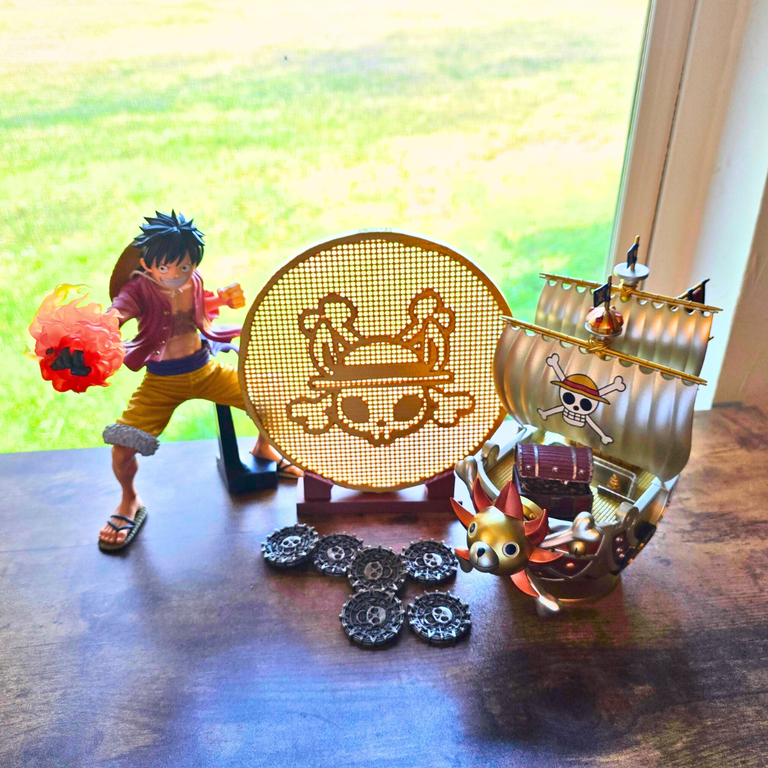 Gold pirate bunny coin enamel pin display board next to some pirate coins and a pirate ship on top of a desk.  An anime guy figure is near the enamel pin board as well 