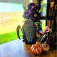 Black Scythe Coffin with Skulls Enamel pin board on top of a desk next to some eyeball flowers, an orange glass pumpkin, and a gothic girl anime figure.