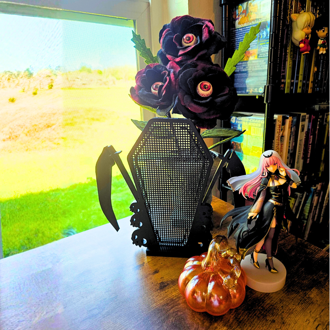 Black Scythe Coffin with Skulls Enamel pin board on top of a desk next to some eyeball flowers, an orange glass pumpkin, and a gothic girl anime figure.