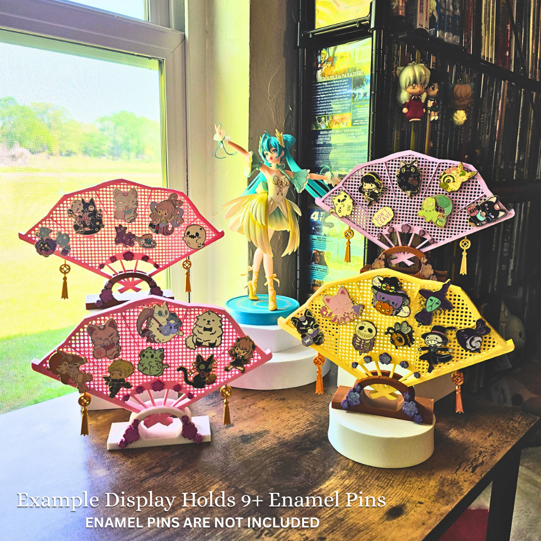 Different 4 colored fans with enamel pins on them, on top of a desk in a room with a blue haired anime girl figure and the words 7 Variety in a cloud, Example display holds 9+ Enamel Pins, Enamel Pins are not included.