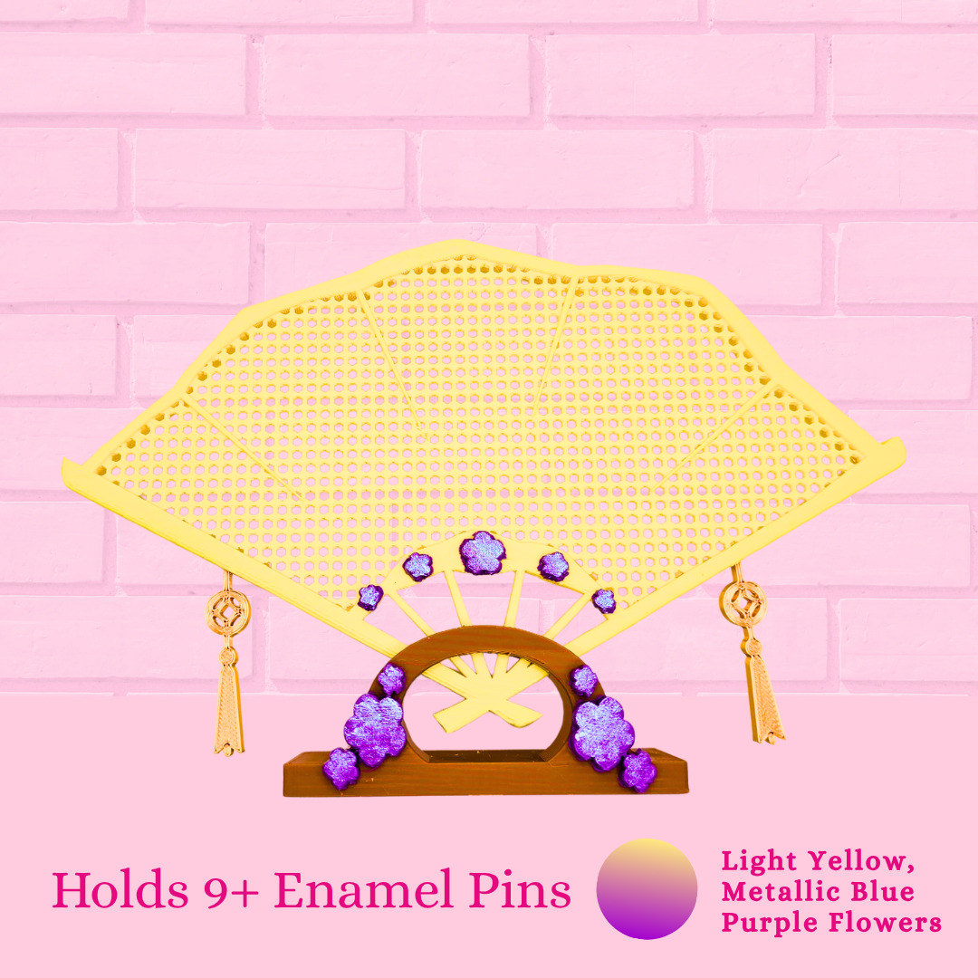 Light yellow Japanese fan close up with the words holds 9+ enamel pins.