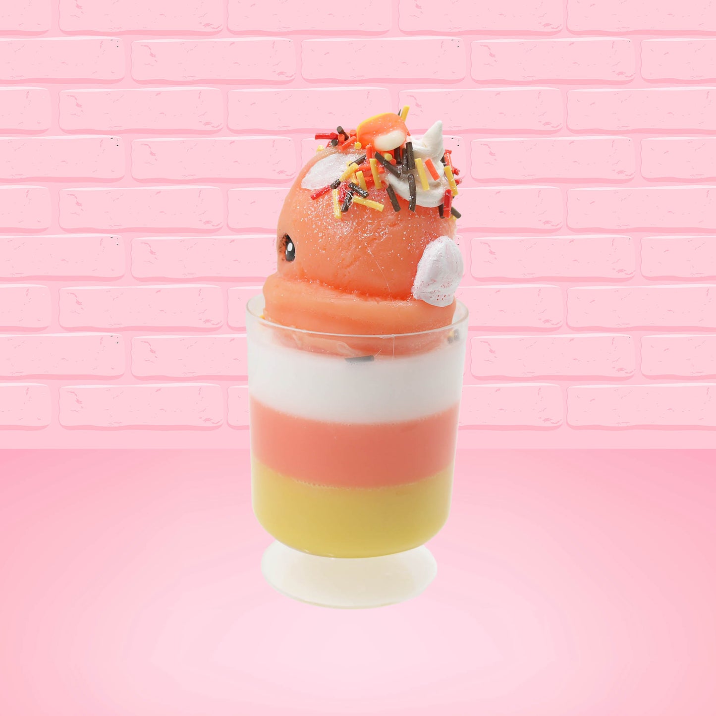 Cute kawaii bunny tall orange, white, and yellow ice cream sundae with yellow, brown, and orange sprinkles on top.  The top also has two pieces of candy corn near the whipped cream swirl. This view is from the back at an angle.