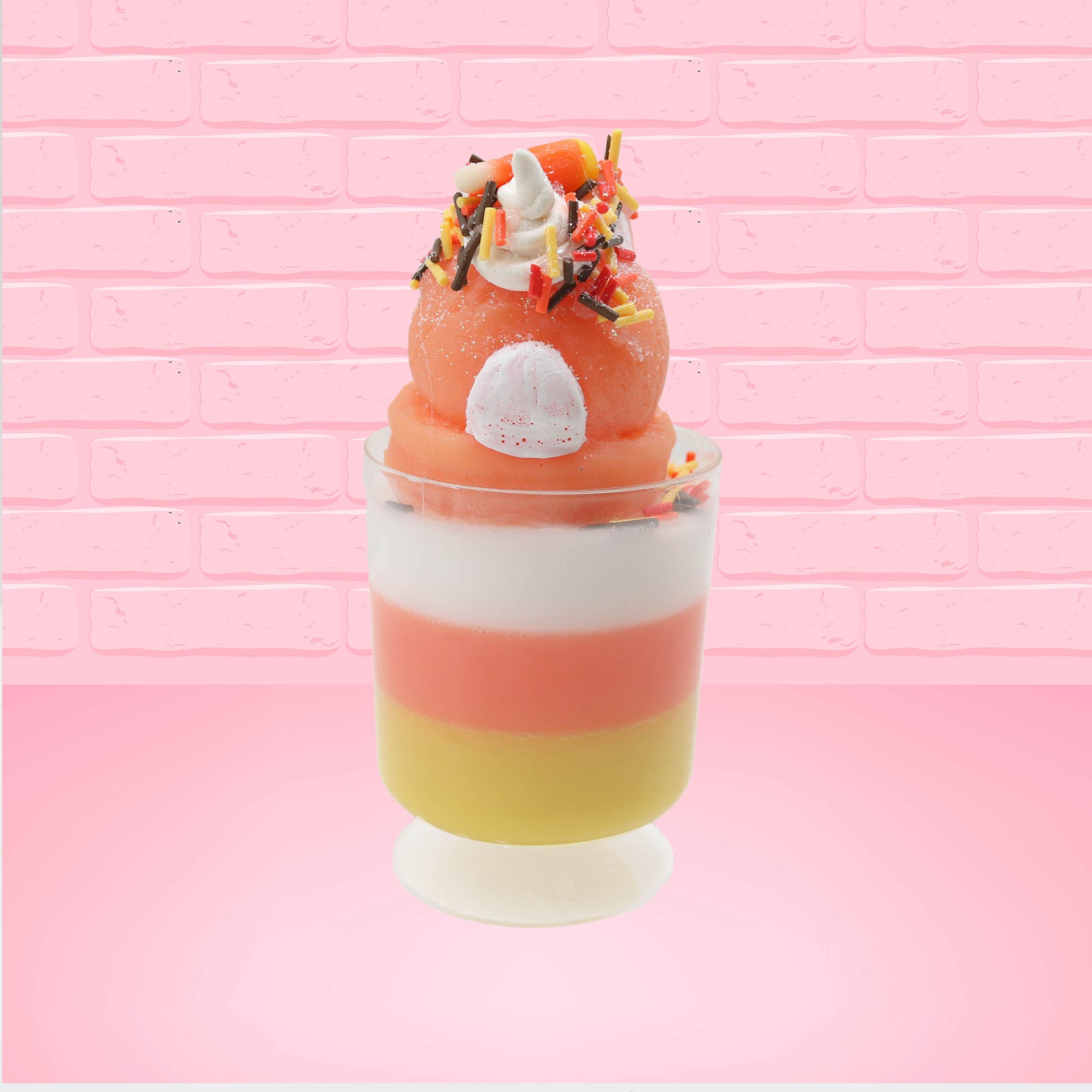 Cute kawaii bunny tall orange, white, and yellow ice cream sundae with yellow, brown, and orange sprinkles on top.  The top also has two pieces of candy corn near the whipped cream swirl. This view is from the back.