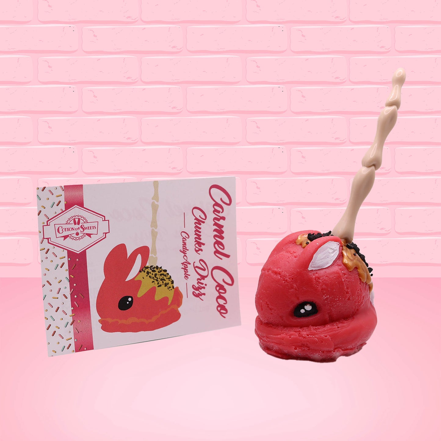 Cute kawaii red bunny with a caramel drizzle with coco bits with a boney finger as a stick. The front of the character card is shown.