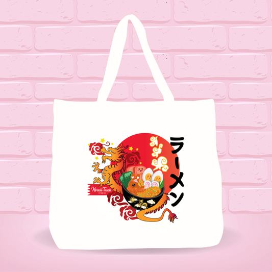 White tote bag with Golden Dragon Sunset Ramen Bunny bowl design and japanese text on a pink brick wall background.