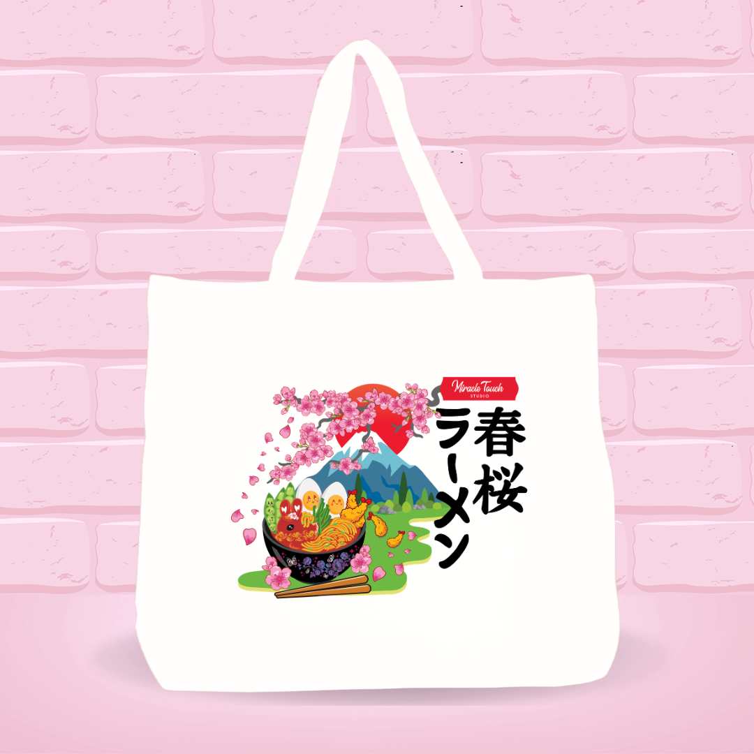 White tote bag with Spring Cherry Blossom Ramen Bunny bowl design and japanese text on a pink brick wall background.