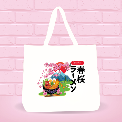 White tote bag with Spring Cherry Blossom Ramen Bunny bowl design and japanese text on a pink brick wall background.