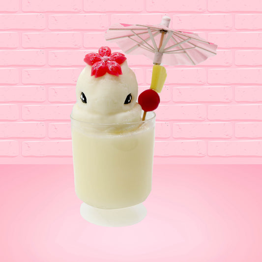 Cute kawaii bunny Pina Colada white drink with a red glittery flower on the top of the bunny in the tall glass. A pink umbrella with a piece of pineapple and cherry sits inside the rim on the side. This view is from the front.