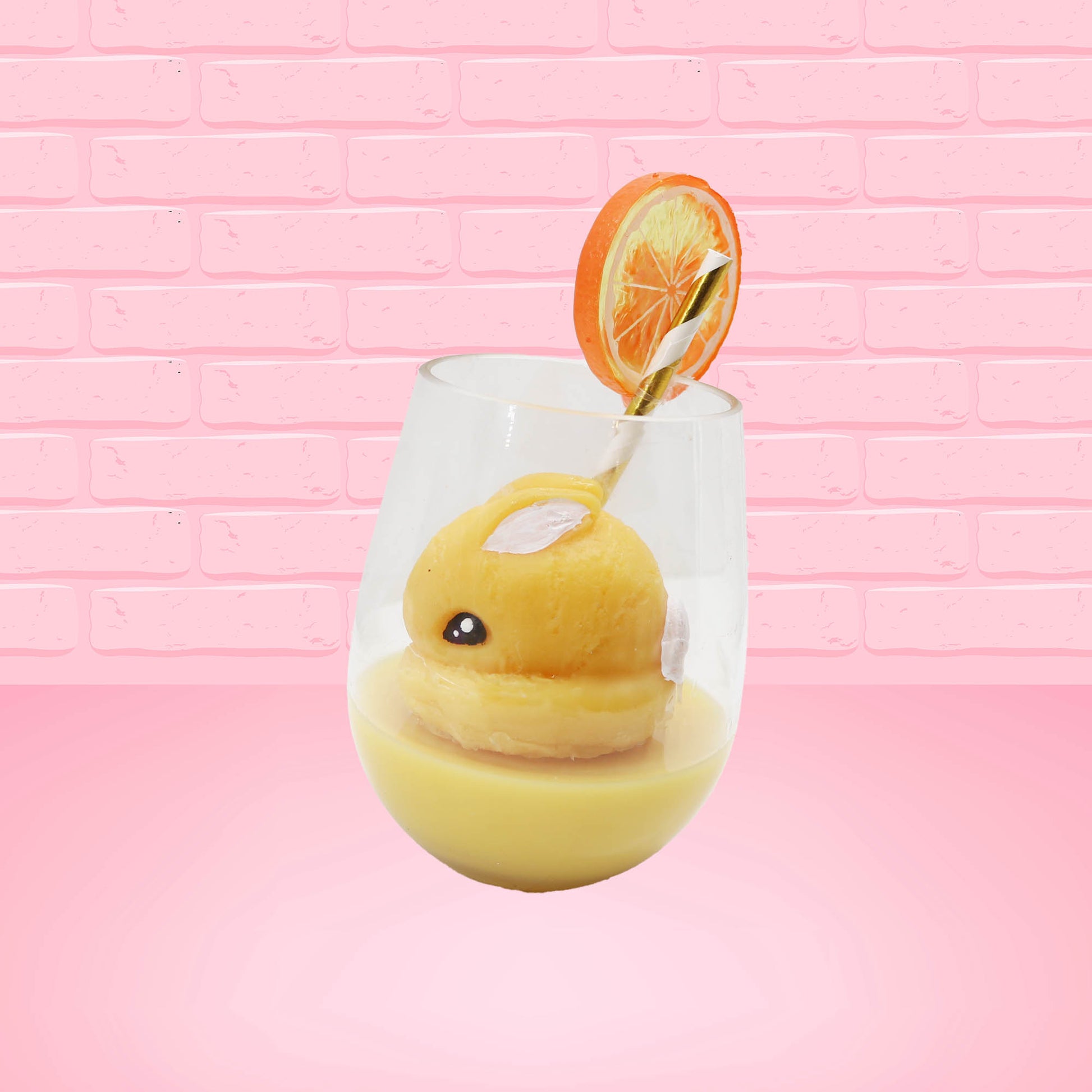 Cute kawaii bunny Screwdriver orange drink inside a glass with a gold white straw with an orange slice and orange flower on the rim of the glass. The view is from the side.