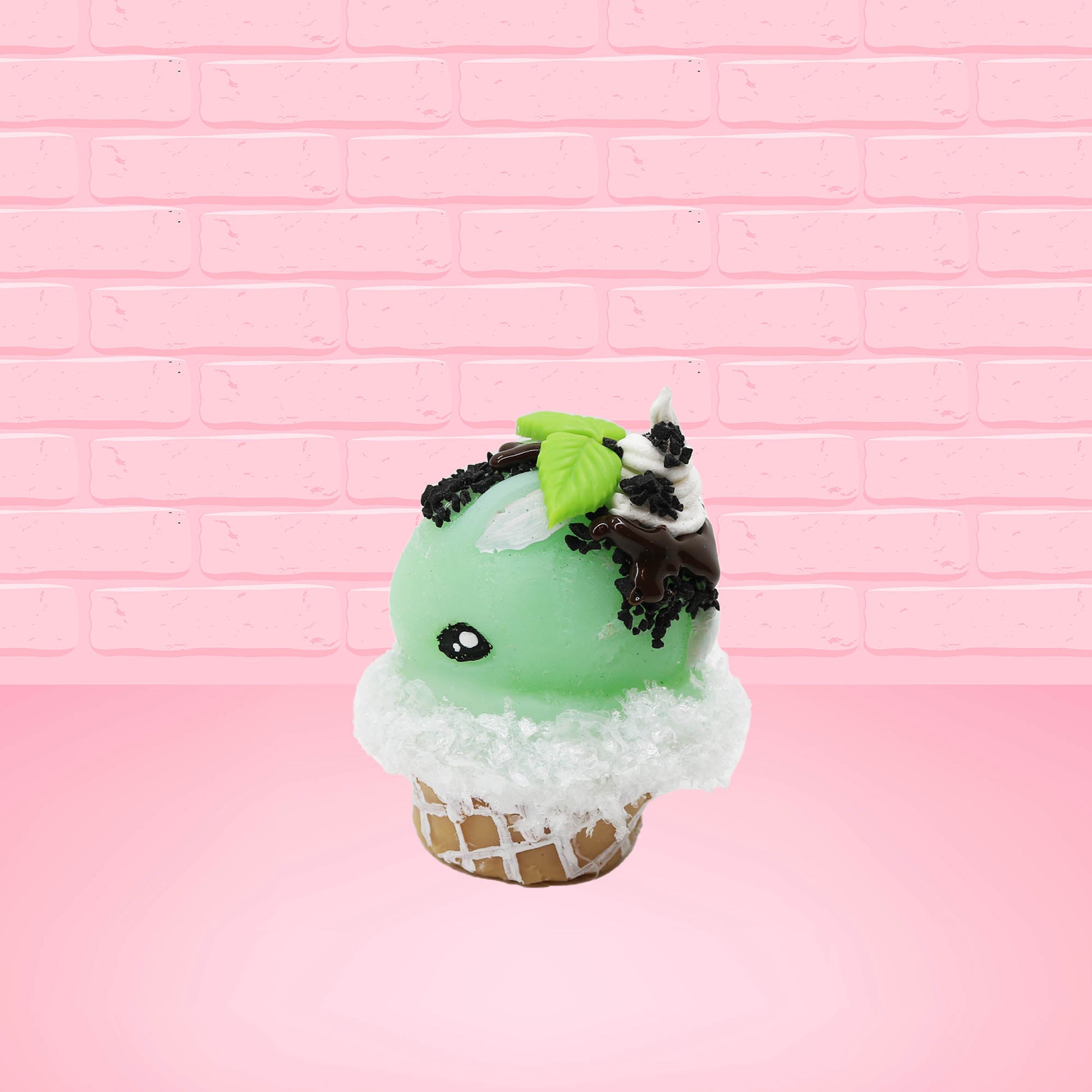 Cute kawaii bunny mint chocolate green ice cream cone with chocolate drizzle and sprinkles near the swirl of the whipped cream, with green mint leaves.  The view is from the other side.