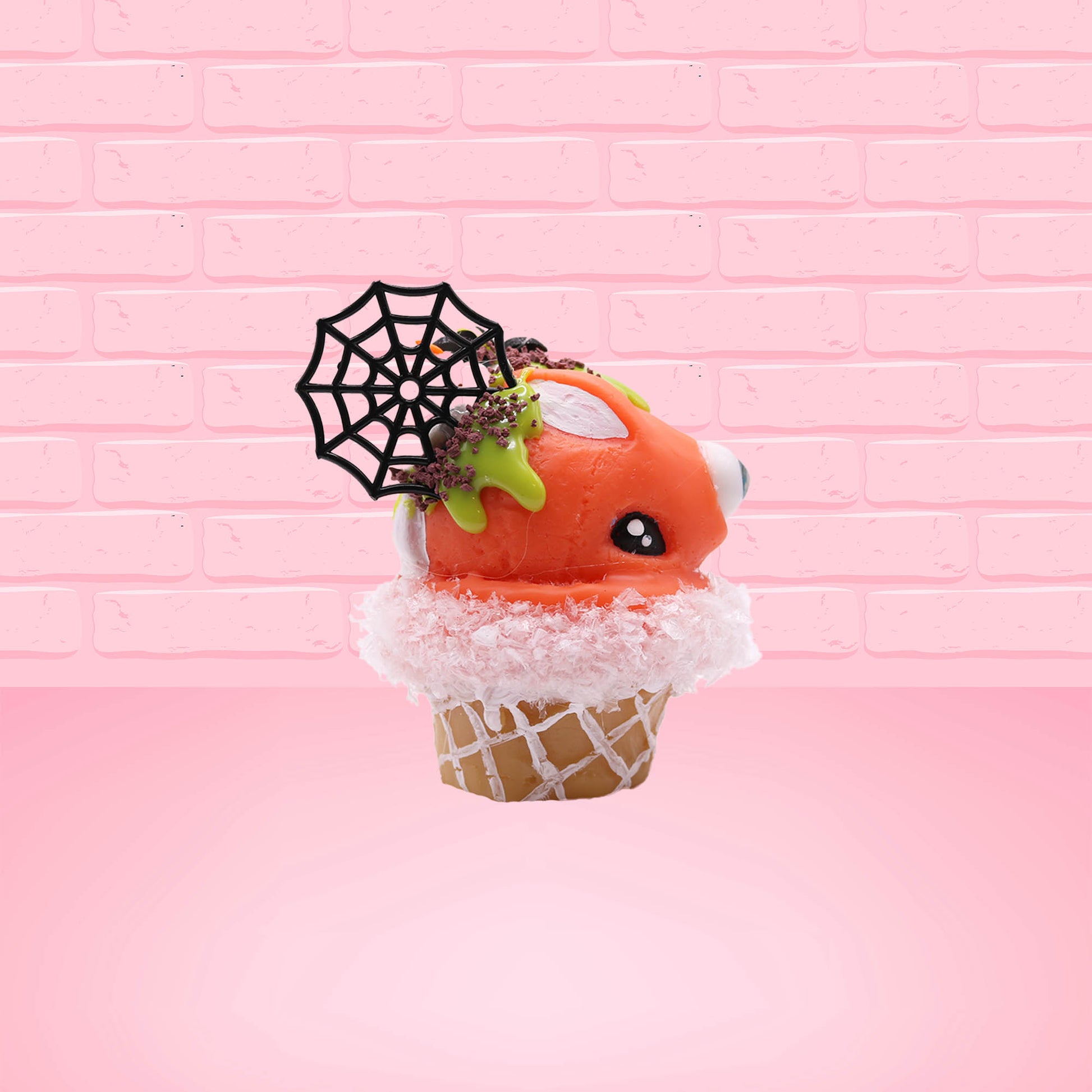 Cute kawaii bunny Monster Scoop orange ice cream cone with a blue eye in the center, green drizzle with chocolate bits, pumpkin sprinkles, a black spider and web near the top of the bunny next to swirl of the whipped cream. This view is from the side.