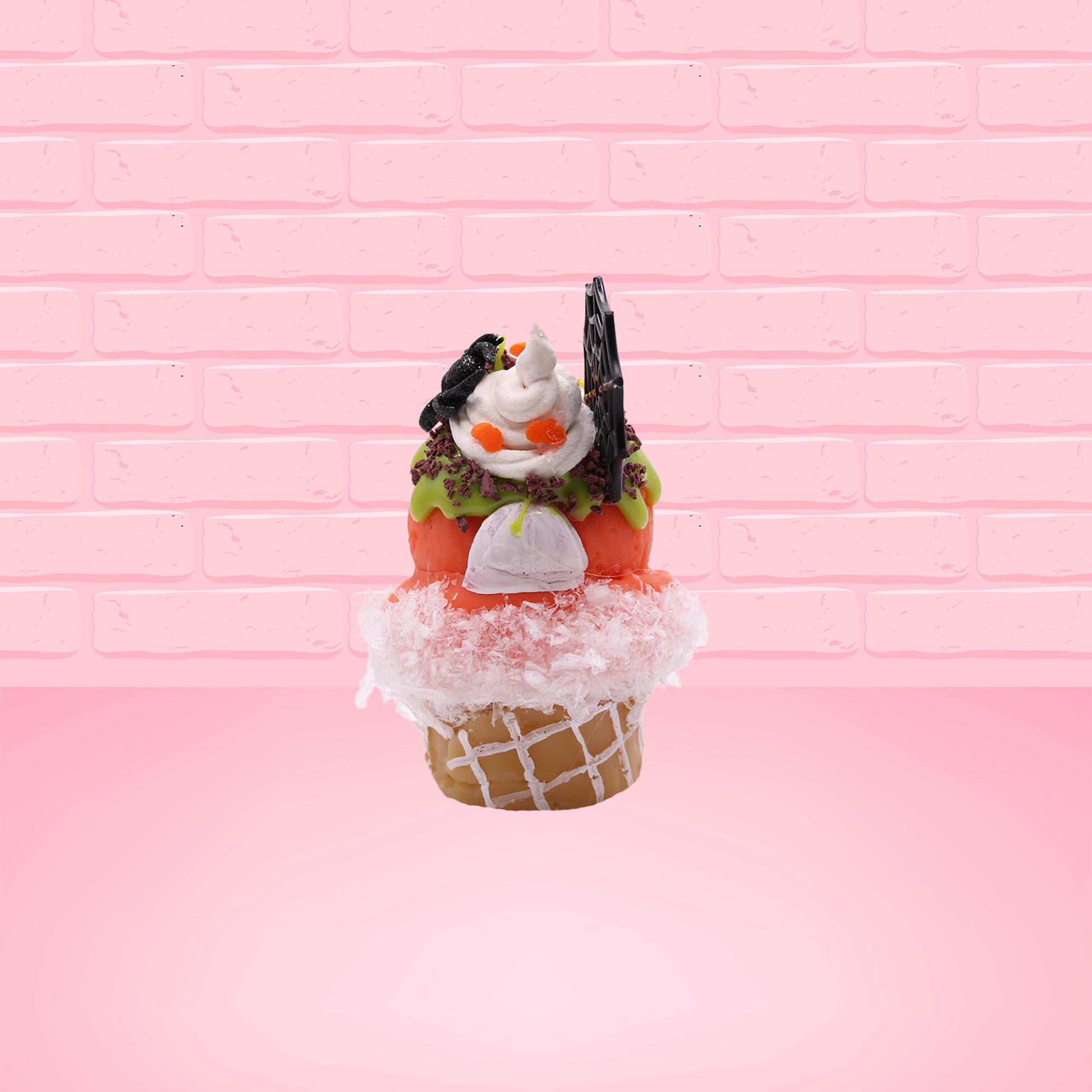 Cute kawaii bunny Monster Scoop orange ice cream cone with a blue eye in the center, green drizzle with chocolate bits, pumpkin sprinkles, a black spider and web near the top of the bunny next to swirl of the whipped cream. This view is from the back.
