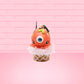 Cute kawaii bunny Monster Scoop orange ice cream cone with a blue eye in the center, green drizzle with chocolate bits, pumpkin sprinkles, a black spider and web near the top of the bunny next to swirl of the whipped cream. This view is from the front.