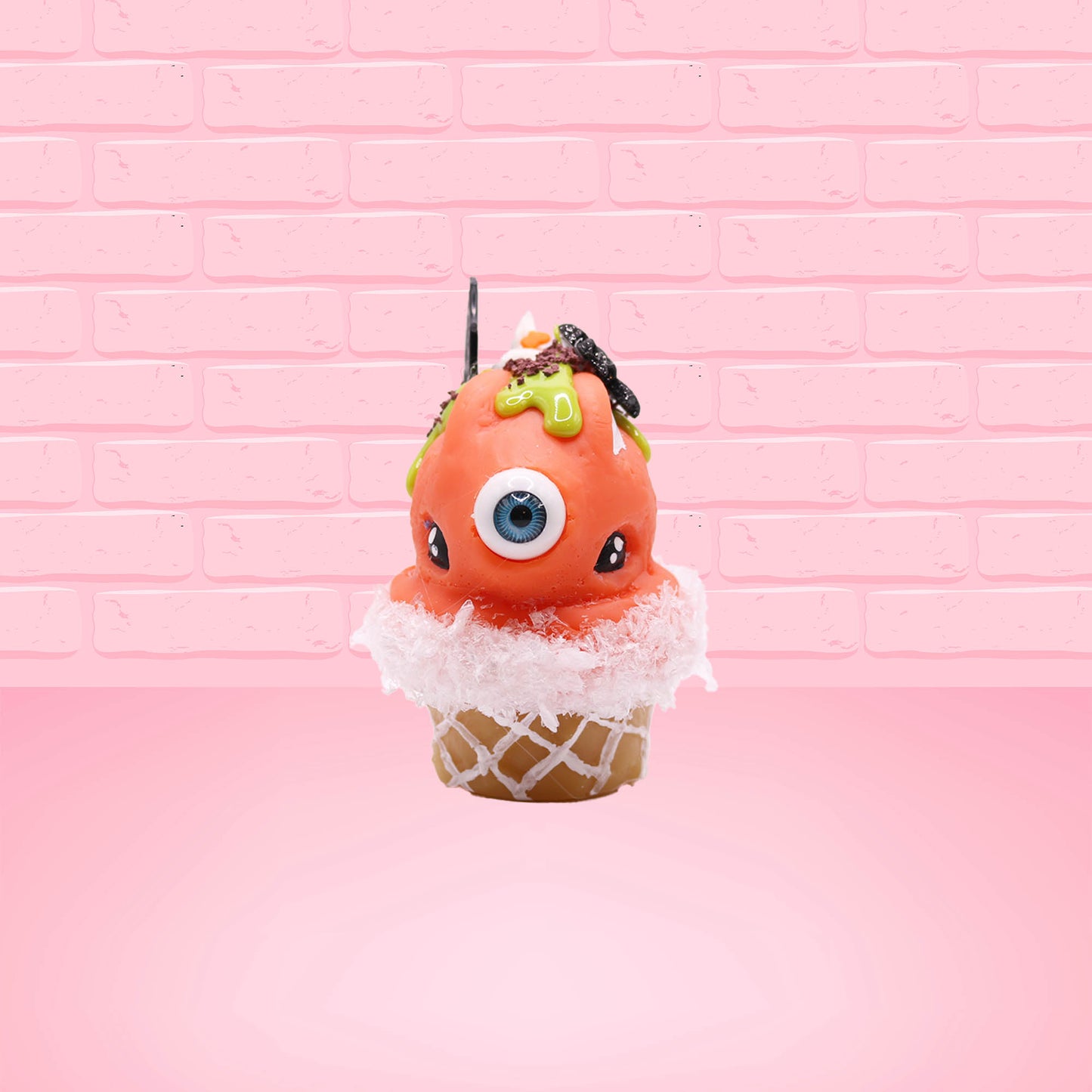 Cute kawaii bunny Monster Scoop orange ice cream cone with a blue eye in the center, green drizzle with chocolate bits, pumpkin sprinkles, a black spider and web near the top of the bunny next to swirl of the whipped cream. This view is from the front.