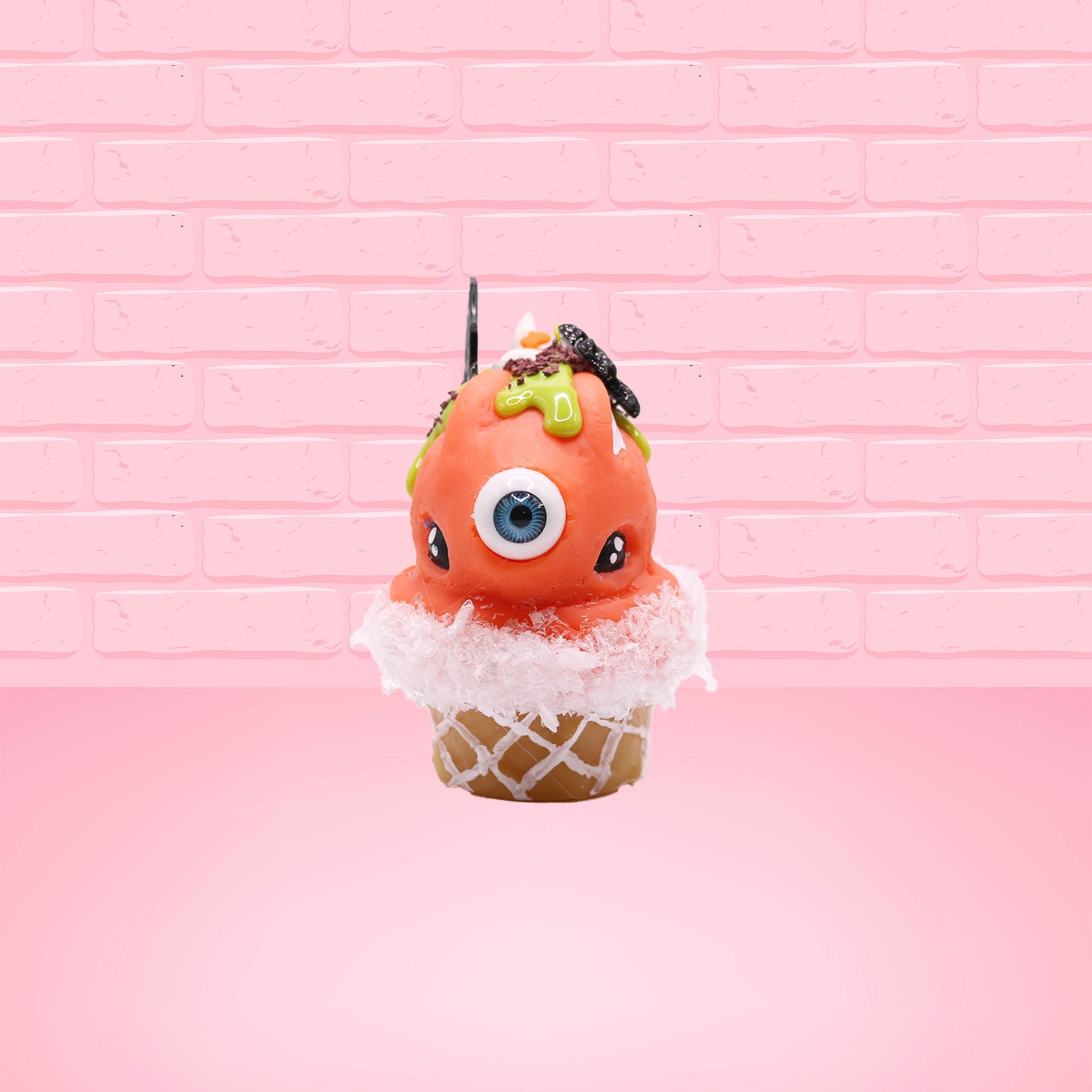 Cute kawaii bunny Monster Scoop orange ice cream cone with a blue eye in the center, green drizzle with chocolate bits, pumpkin sprinkles, a black spider and web near the top of the bunny next to swirl of the whipped cream. This view is from the front.