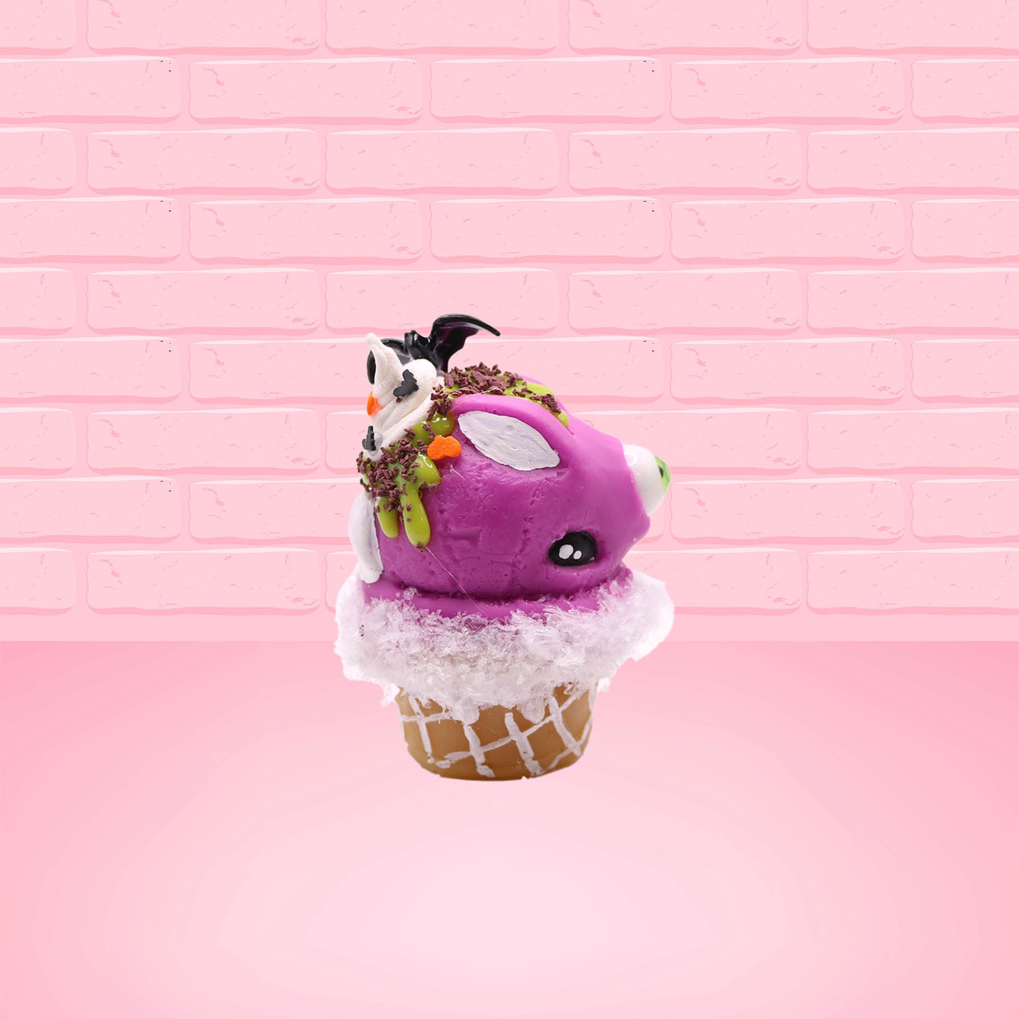 Cute kawaii bunny Monster Scoop purple ice cream cone with a green eye in the center, green drizzle with chocolate bits, pumpkin and bat sprinkles, and a bat on the top of the bunny near the whipped cream swirl. This view is from the other side.