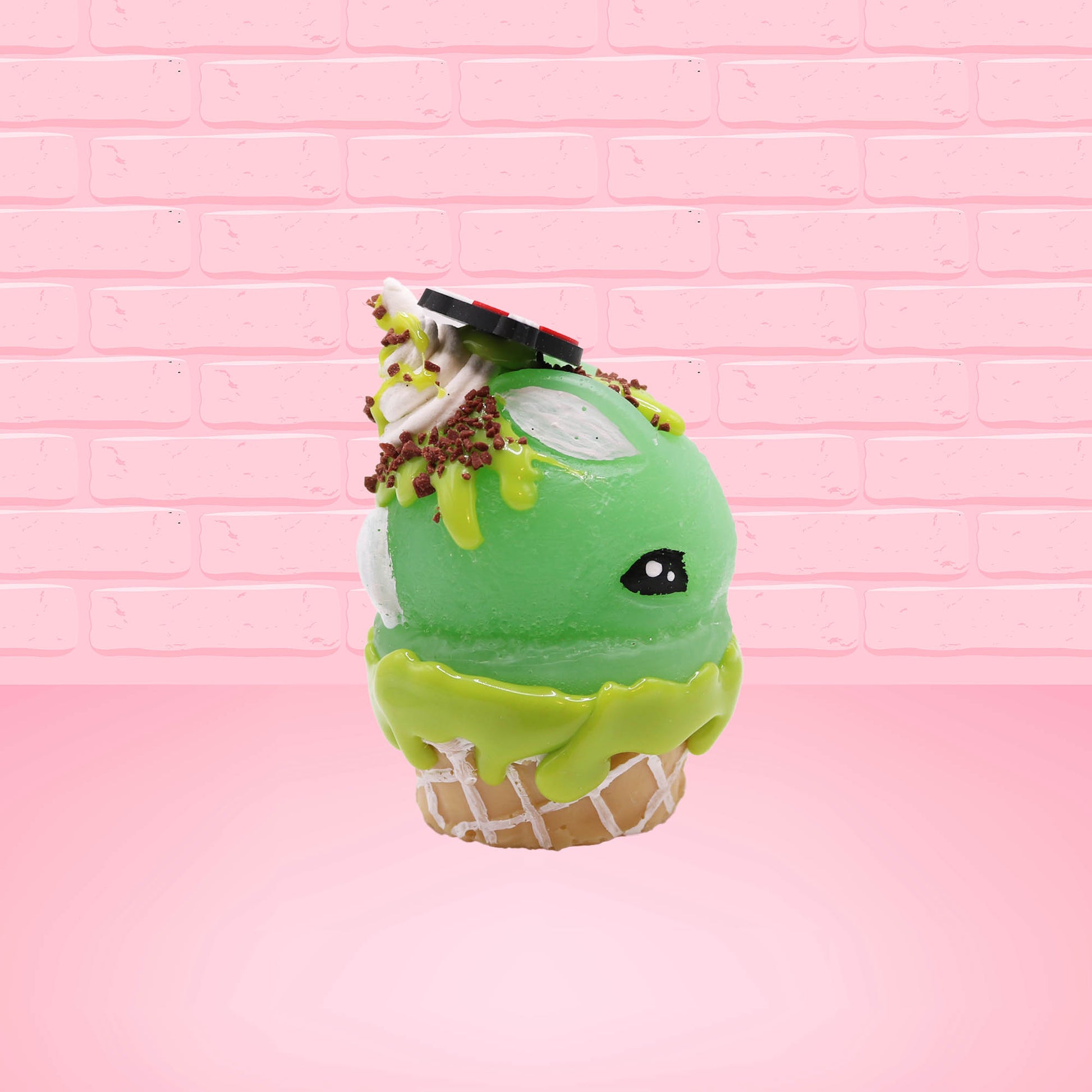 Cute kawaii bunny Slimer Scoop green ice cream cone with green drizzle and brown bits, a ghost buster logo near the whipped cream swirl on top. This view is from the other side.