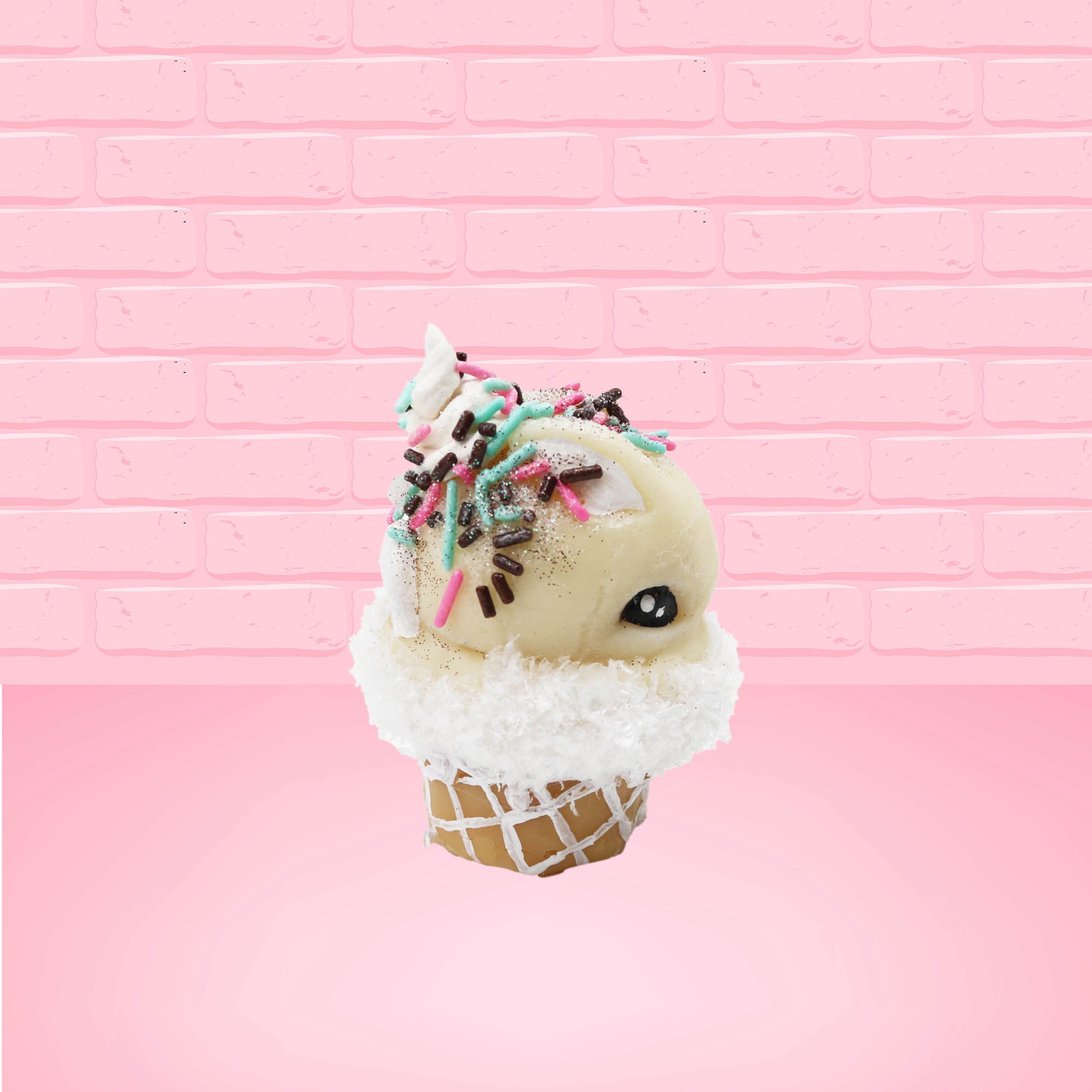 Cute kawaii bunny white ice cream cone with pink, teal, and black sprinkles on top of the bunny near the whipped cream swirl. The view is from the other side. 