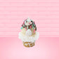 Cute kawaii bunny white ice cream cone with pink, teal, and black sprinkles on top of the bunny near the whipped cream swirl. The view is from the back. 