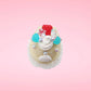 Cute kawaii bunny Vanilla Star Blast white ice cream cone with a blueberry, raspberry, and silver pearls near the swirl of whipped cream on the top of the bunny. This view is from the top.