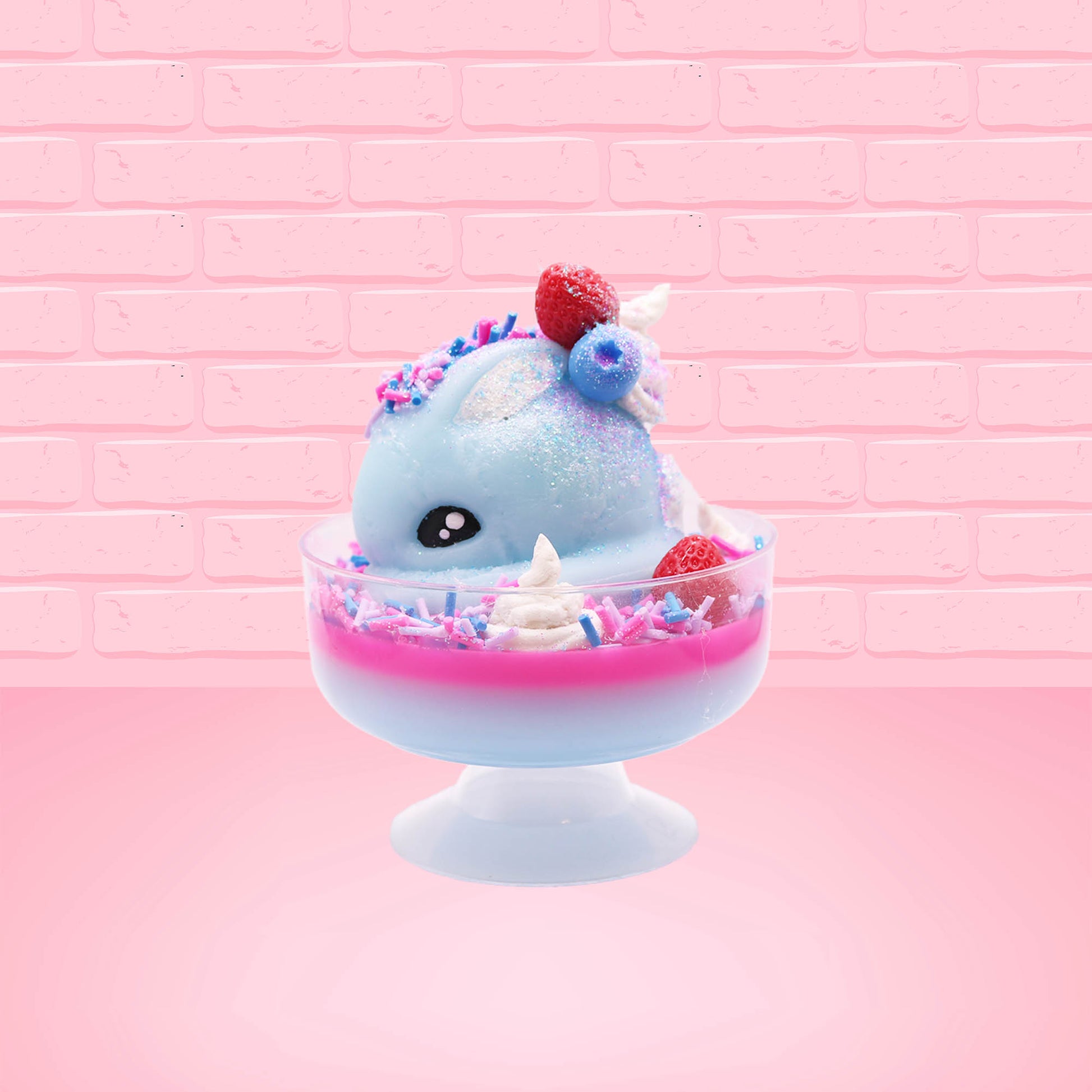 Cute kawaii Berry Swirl Cotton Candy blue ice cream sundae with pink glaze, pink blue and white sprinkles, strawberries and whipped cream swirls in the dish.  There are sprinkles, a blue berry, and strawberry on the top of the bunny near the swirl of the whipped cream. This view is from the side.