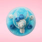 Cute kawaii Blue Berry Cotton Candy ice cream sundae with blue berries and swirls of whipped cream in the dish, while covered with blue glitter.  The bunny has two blue berries on the top near the swirl of whipped cream on the back. This view is from the top.