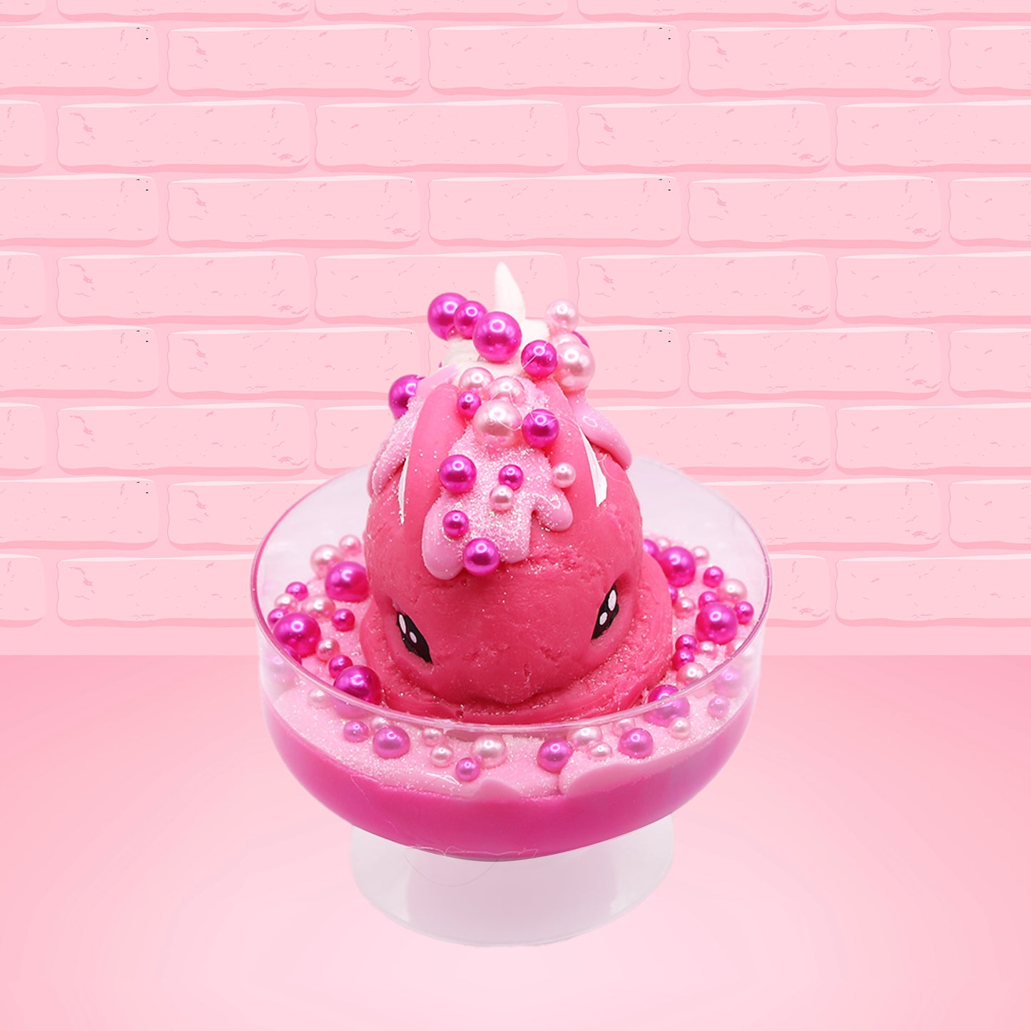 Cute kawaii bunny Bubbles pink ice cream sundae with light pink drizzle, pink and hot pink metallic spheres inside the dish. The bunny’s top is covered with the pink and hot pink spheres as well as a swirl of whipped cream. This view is from the front.