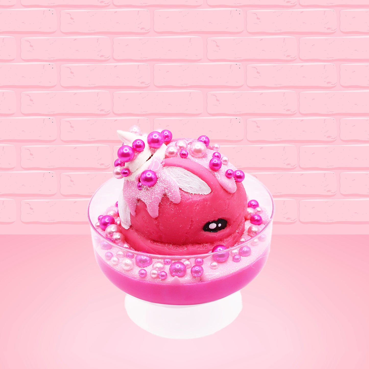 Cute kawaii bunny Bubbles pink ice cream sundae with light pink drizzle, pink and hot pink metallic spheres inside the dish. The bunny’s top is covered with the pink and hot pink spheres as well as a swirl of whipped cream. This view is from the side.