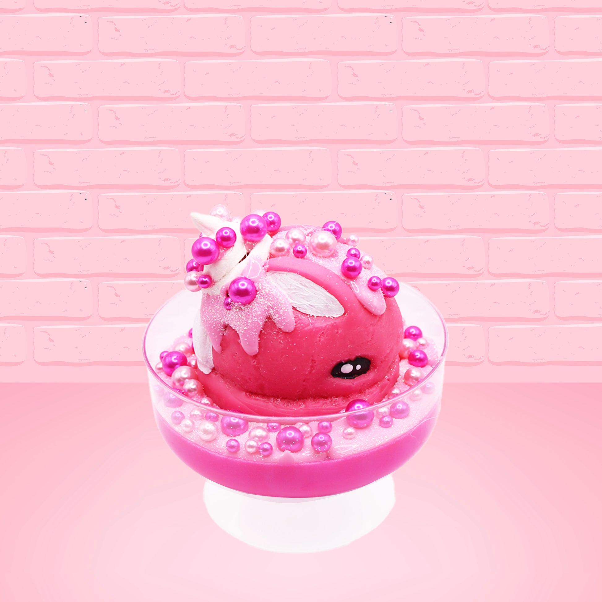 Cute kawaii bunny Bubbles pink ice cream sundae with light pink drizzle, pink and hot pink metallic spheres inside the dish. The bunny’s top is covered with the pink and hot pink spheres as well as a swirl of whipped cream. This view is from the side.