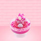Cute kawaii bunny Bubbles pink ice cream sundae with light pink drizzle, pink and hot pink metallic spheres inside the dish. The bunny’s top is covered with the pink and hot pink spheres as well as a swirl of whipped cream. This view is from the back. 