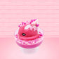 Cute kawaii bunny Bubbles pink ice cream sundae with light pink drizzle, pink and hot pink metallic spheres inside the dish. The bunny’s top is covered with the pink and hot pink spheres as well as a swirl of whipped cream. This view is from the other side.