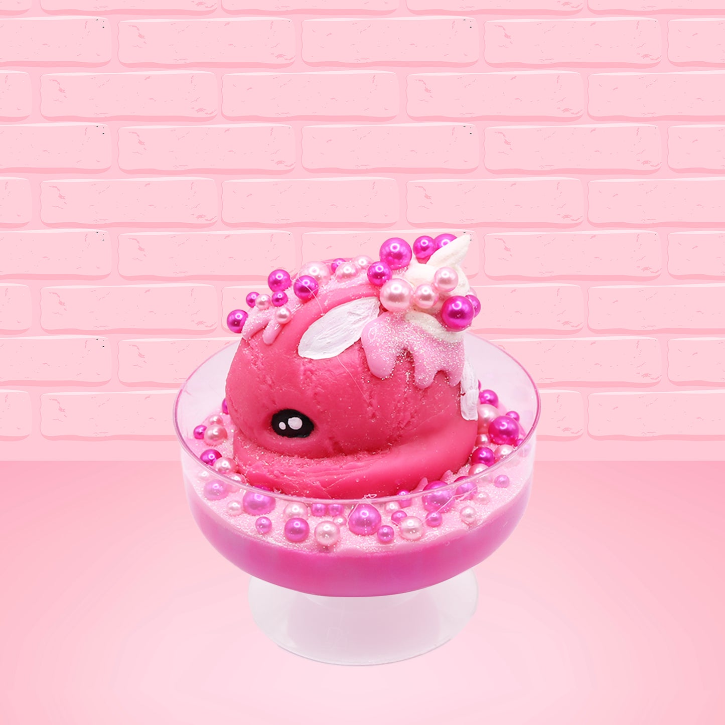 Cute kawaii bunny Bubbles pink ice cream sundae with light pink drizzle, pink and hot pink metallic spheres inside the dish. The bunny’s top is covered with the pink and hot pink spheres as well as a swirl of whipped cream. This view is from the other side.