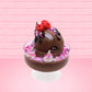 Cute kawaii bunny Chocolate Rush brown ice cream sundae with pink and purple sprinkles with swirls of whipped cream in the dish. The bunny has raspberries, chocolate glittery drizzle and sprinkles on top near the whipped cream swirl. This view is from the side.