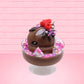 Cute kawaii bunny Chocolate Rush brown ice cream sundae with pink and purple sprinkles with swirls of whipped cream in the dish. The bunny has raspberries, chocolate glittery drizzle and sprinkles on top near the whipped cream swirl. This view is from the other side.