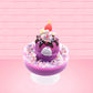 Cute kawaii unicorn bunny Coco Dazzle Star purple ice cream with pink, purple and white sprinkles with swirls of whipped cream in the dish. The unicorn bunny has a strawberry and banana slices with chocolate drizzle and sprinkles near the whipped cream swirl. This view is from the back.
