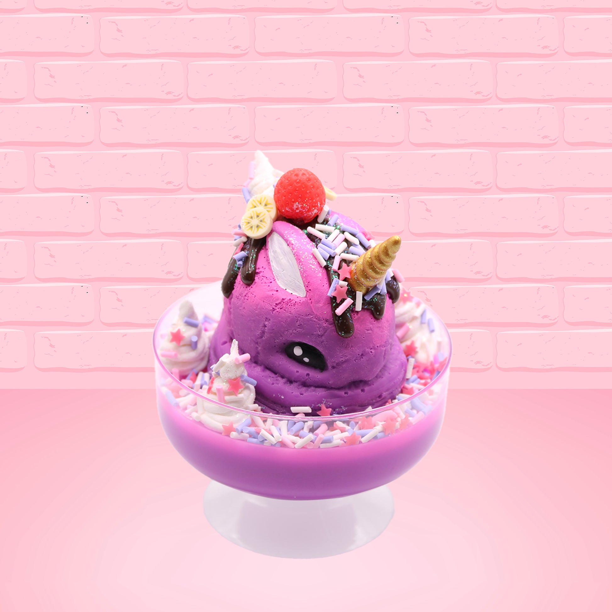 Cute kawaii unicorn bunny Coco Dazzle Star purple ice cream with pink, purple and white sprinkles with swirls of whipped cream in the dish. The unicorn bunny has a strawberry and banana slices with chocolate drizzle and sprinkles near the whipped cream swirl. This view is from the front at an angle.