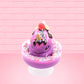 Cute kawaii unicorn bunny Coco Dazzle Star purple ice cream with pink, purple and white sprinkles with swirls of whipped cream in the dish. The unicorn bunny has a strawberry and banana slices with chocolate drizzle and sprinkles near the whipped cream swirl. This view is from the front.