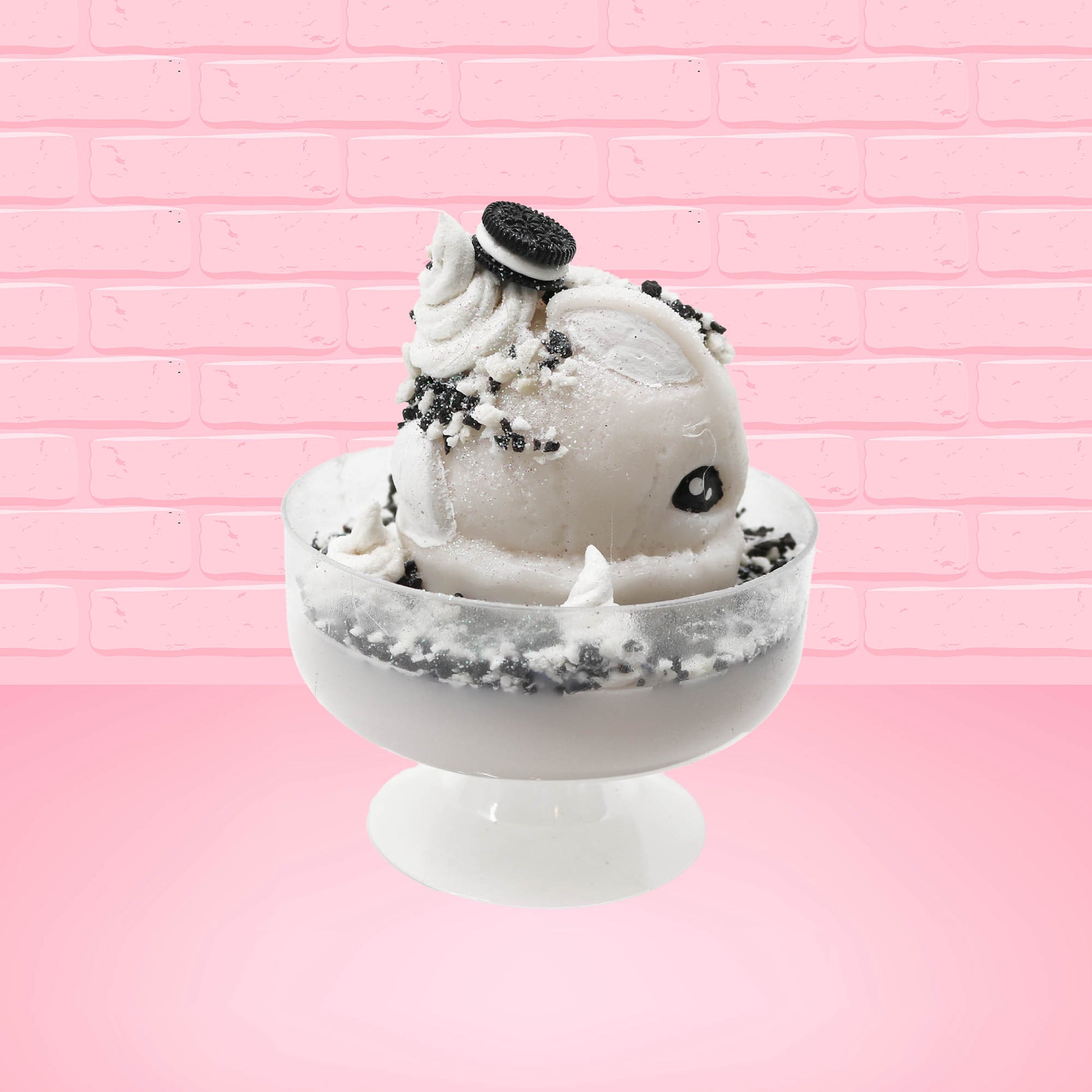 Cute kawaii bunny cookies and cream ice cream white scoop sundae with whipped cream swirls and black white crumbles in the dish. A black and white sandwhich cookie is on top of the resin bunny, sprinkled with black and white crumbles and a swirl of whipped cream. This view is from the other side.