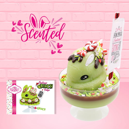 Cute kawaii ice cream Emotional Grinch Fudge sundae which has a sign and green white and red heart sprinkles inside of the dish as well as swirls of whipped cream. The bunny has chocolate glaze, peppermint candies and a swirl of whipped cream on it’s head. The character card front is shown as well as the word scented. 